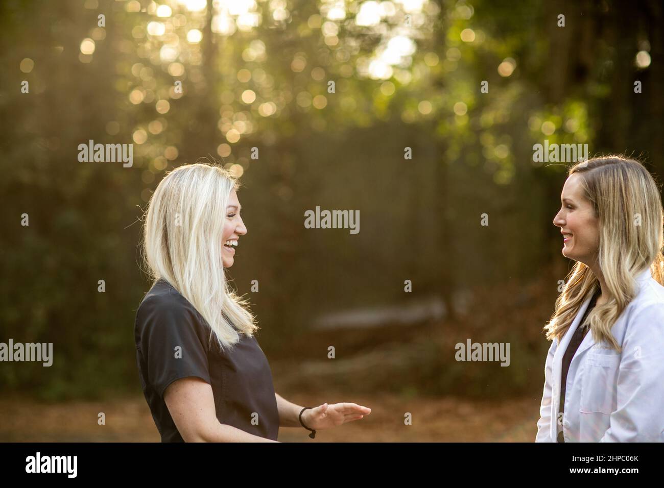 Zwei medizinische Frauen mit schwarzen Peelings und eine trägt einen weißen Laborkittel, der draußen steht und redet Stockfoto