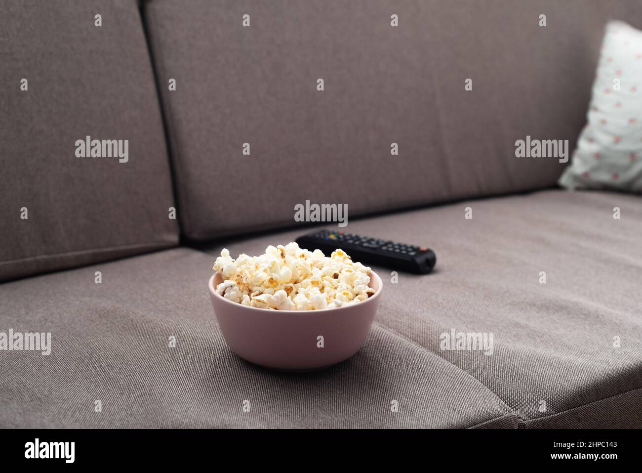 Schüssel mit Popcorn und tv-Fernbedienung auf dem Sofa Stockfoto
