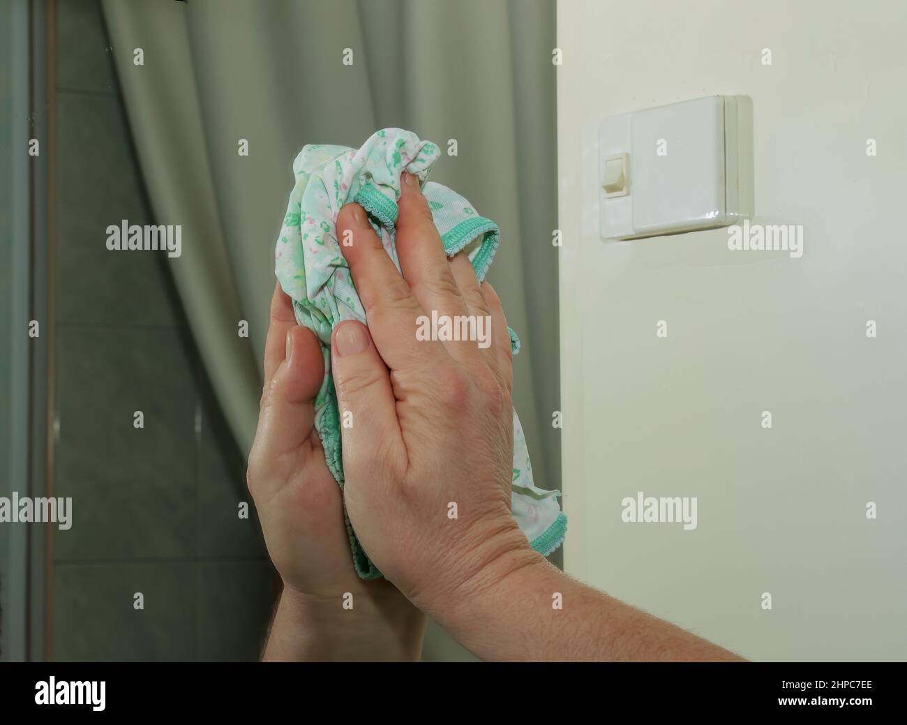 Eine Frau reinigt einen Spiegel mit einer Serviette von Schmutz und Plaque aus Wasser zu Hause. Stockfoto