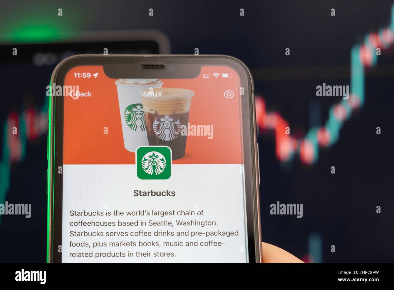 Der Aufwärtstrend der Aktienkursen bei Starbucks mit Grafiken im Hintergrund. Man hands Holding a Smartphone with Logo on the screen, February 2022, San Francisco, USA. Stockfoto
