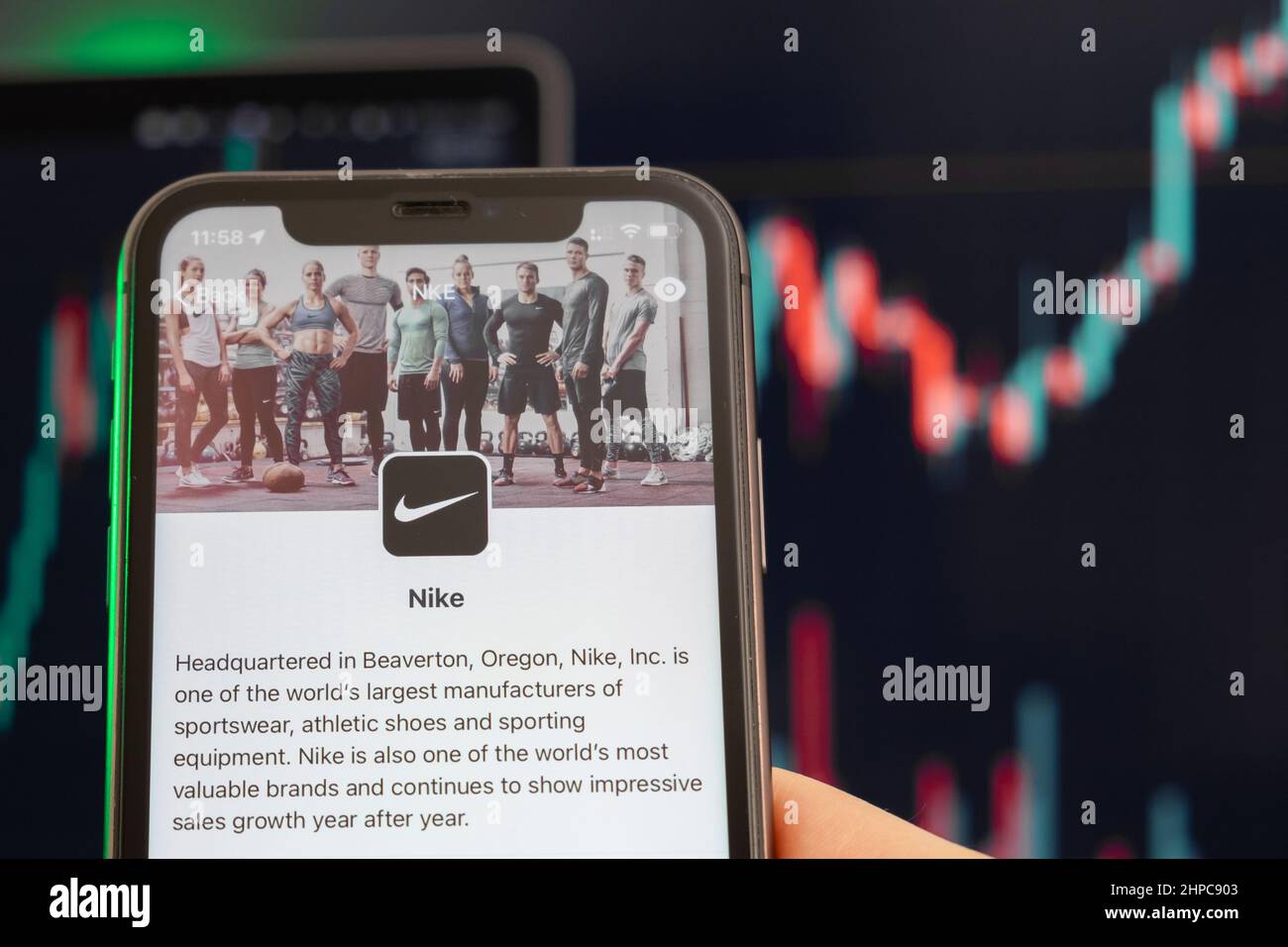 Der Aufwärtstrend der Nike Aktienkursen mit Grafiken im Hintergrund. Man hands Holding a Smartphone with Logo on the screen, February 2022, San Francisco, USA. Stockfoto