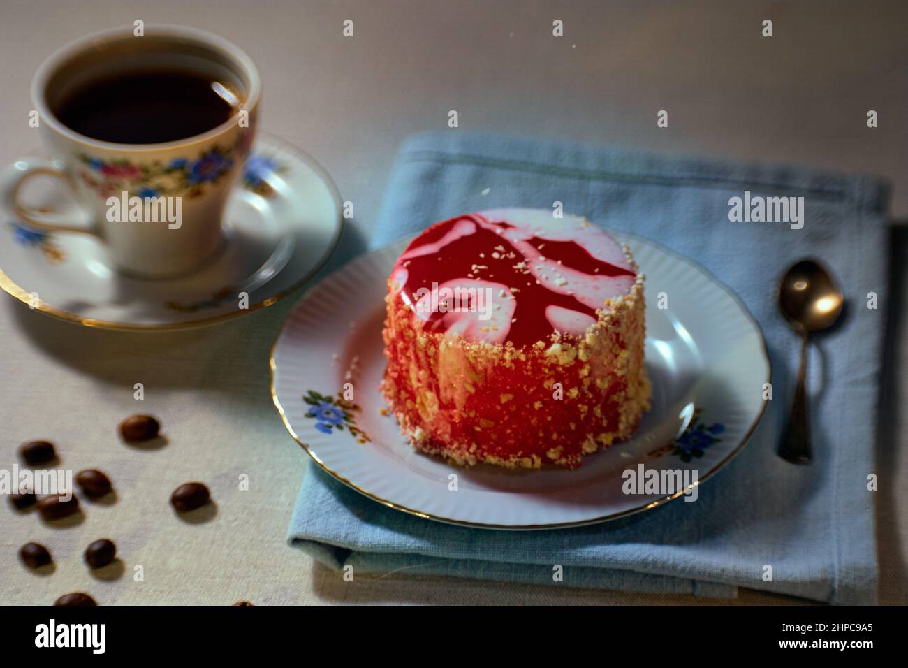 Frühstückskonzept mit Louise-Kuchen auf Keramikplatte, Kaffee in einer Fayence-Tasse auf dem Hintergrund, verstreute Kaffeebohnen auf einem Tisch Stockfoto