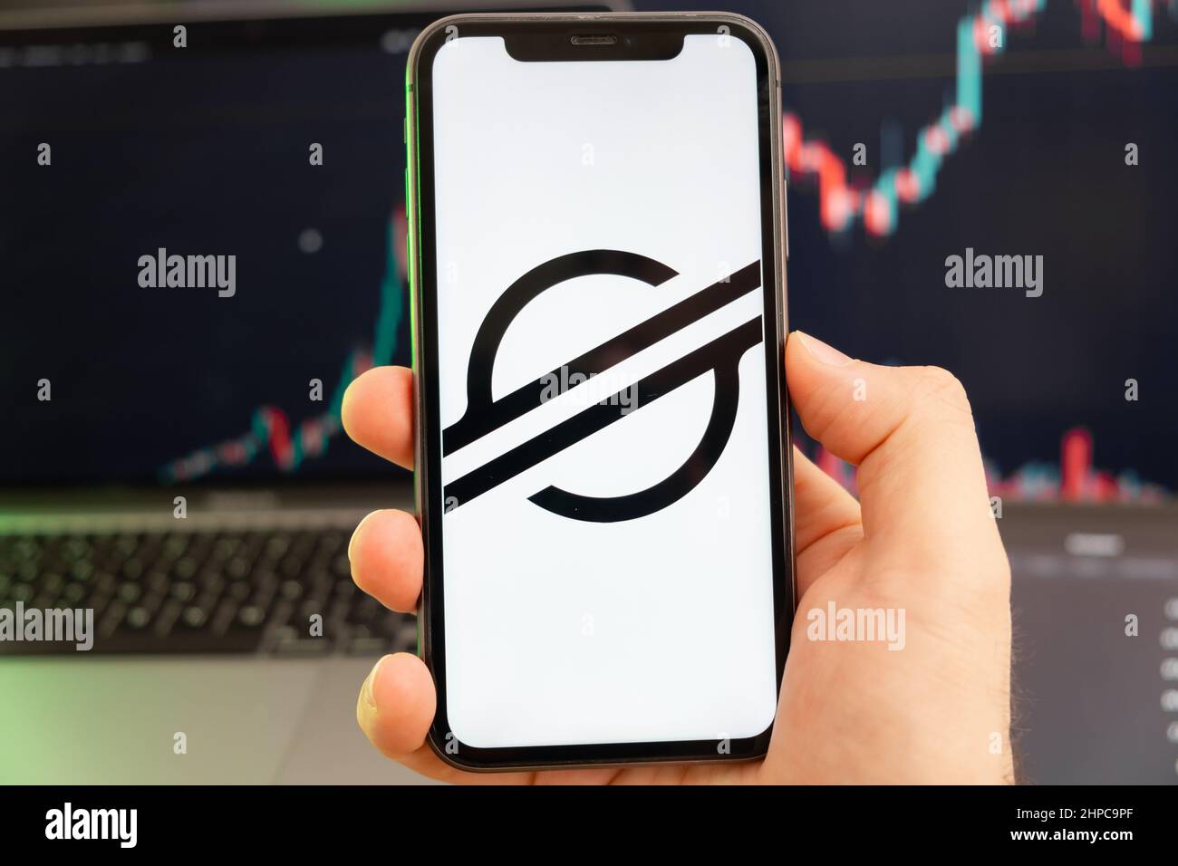 Stellar XLM Kryptowährung Logo auf dem Bildschirm eines Smartphones in mans Hand mit einem wachsenden Trend auf dem Chart auf einem grünen Hintergrund. Stockfoto