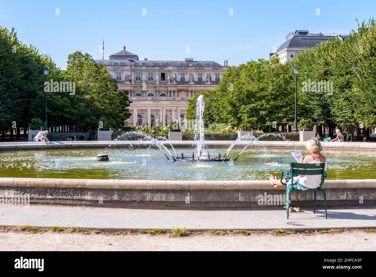 Eine ältere Frau entspannt sich auf einem Metallrasenstuhl am Brunnen im Garten des Palais-Royal in Paris, Frankreich. Stockfoto