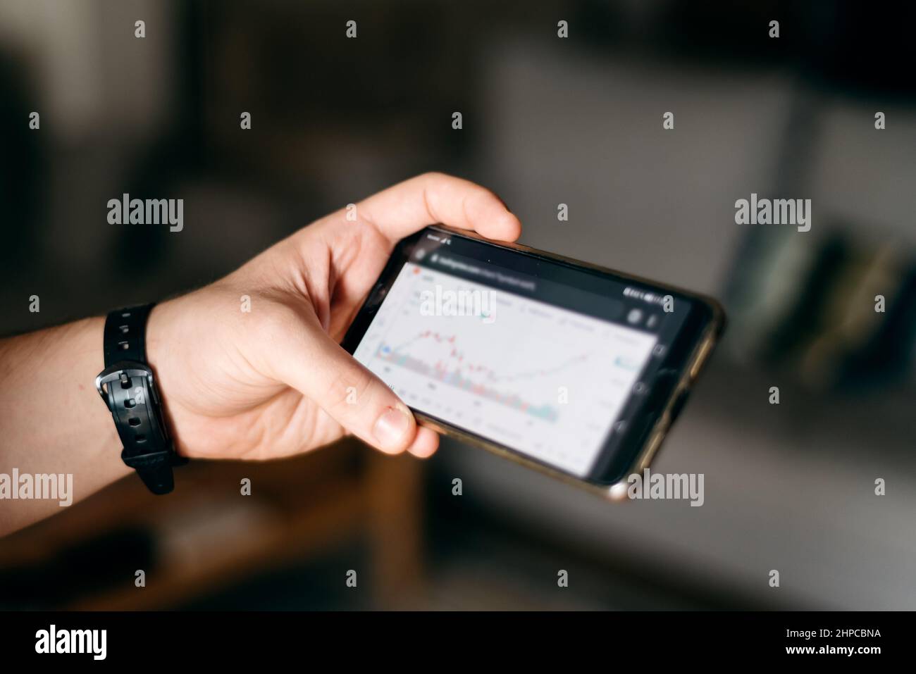 Junger Mann hält sein Handy mit grafischem Chart der Börse. Finanz- und Kryptowährungskonzepte Stockfoto