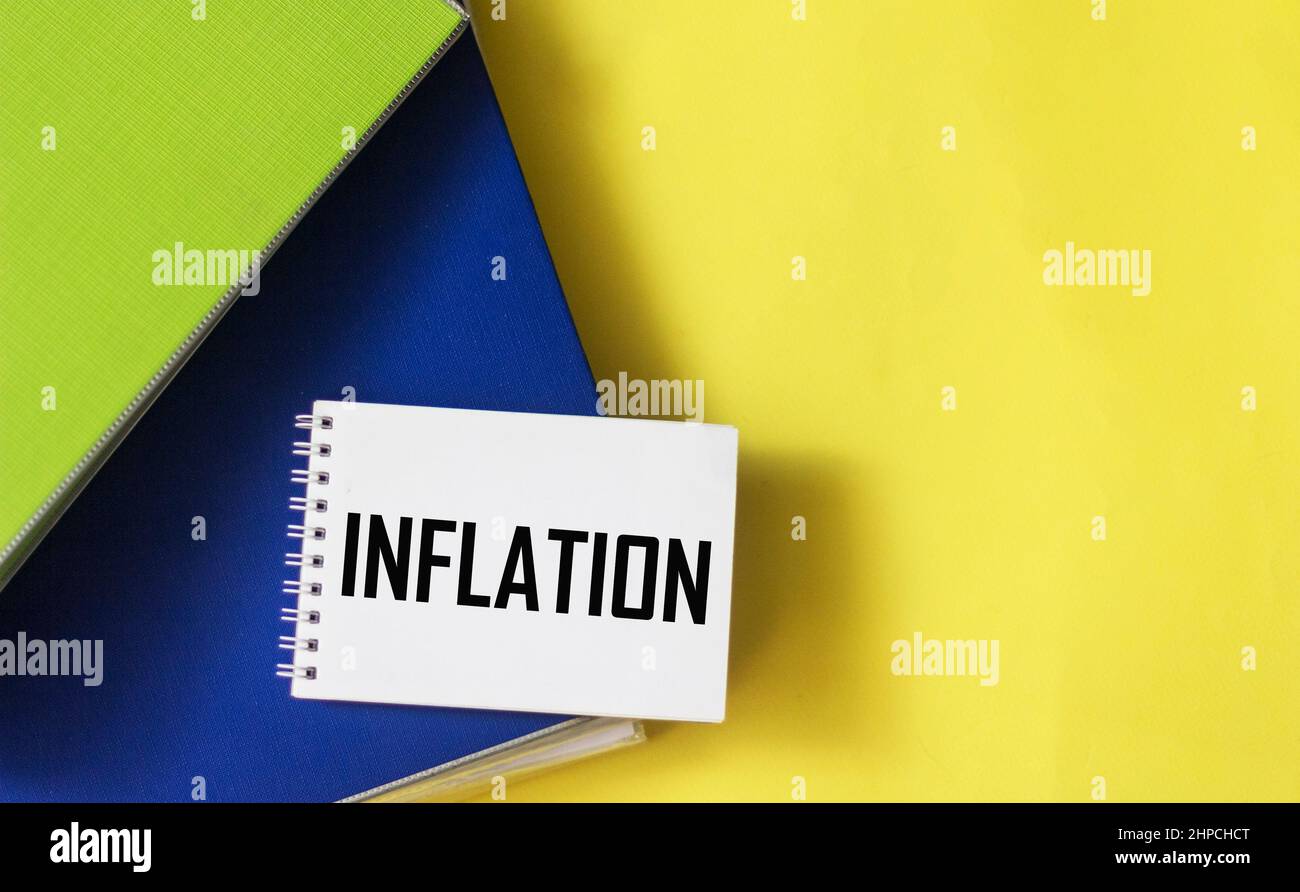 Das Wort Inflation ist auf einem Notizblock und einem gelben Hintergrund mit Ordnern von Dokumenten geschrieben. Stockfoto