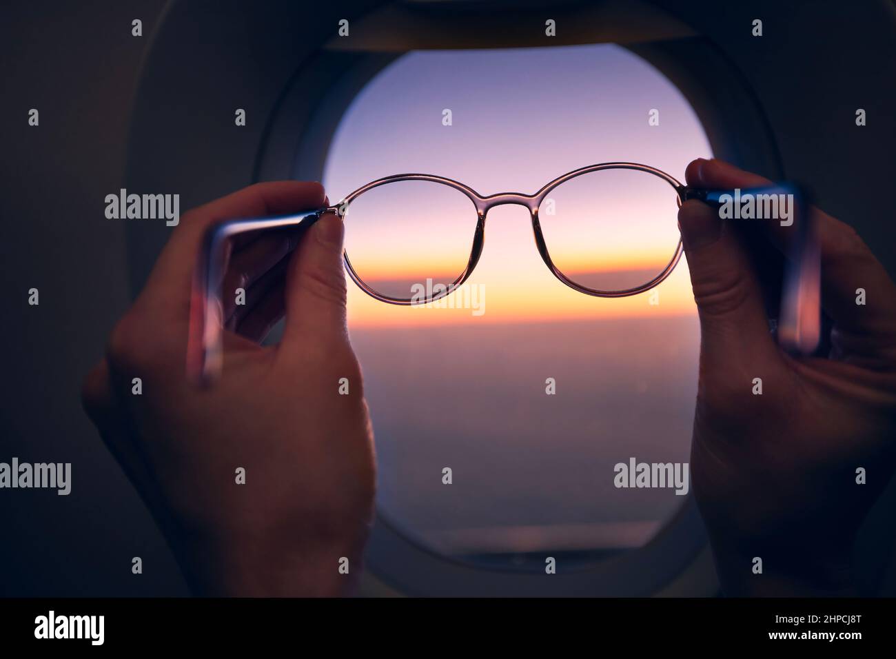 Die Hand des Beifahrers hält bei Sonnenuntergang Brillen gegen das Flugzeugfenster. Themen Reisen, Sehvermögen und Vision. Stockfoto