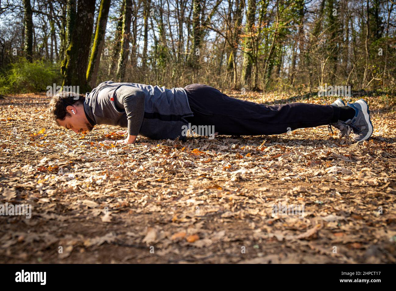 Der Läufer macht Liegestütze im Wald. Der junge Mann mit den blauen Augen und dem Schnurrbart macht Liegestütze auf dem Boden, während er der Musik zuhört Stockfoto