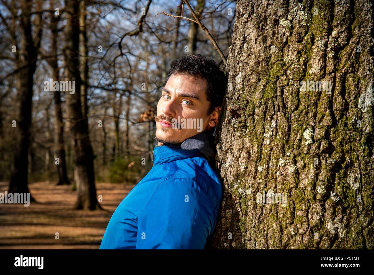Porträt eines schönen jungen Mannes mit blauen Augen. Der Mann trainiert im Wald und lehnt sich an eine Eiche. Stockfoto