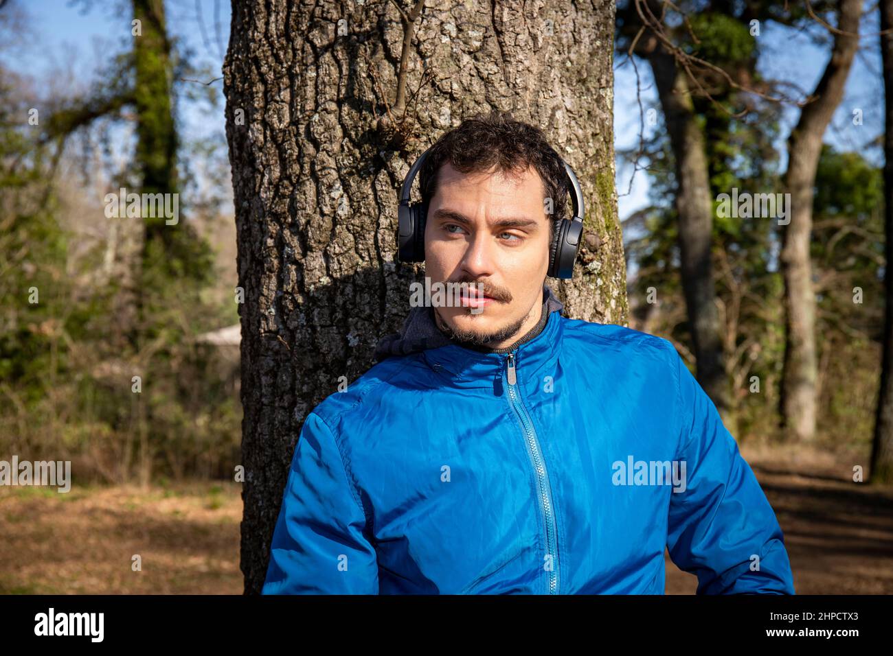 Porträt eines hübschen jungen Mannes mit blauen Augen und einem Schnurrbart, der beim Training Musik hört. Der Mann in der blauen Jacke trainiert in t Stockfoto