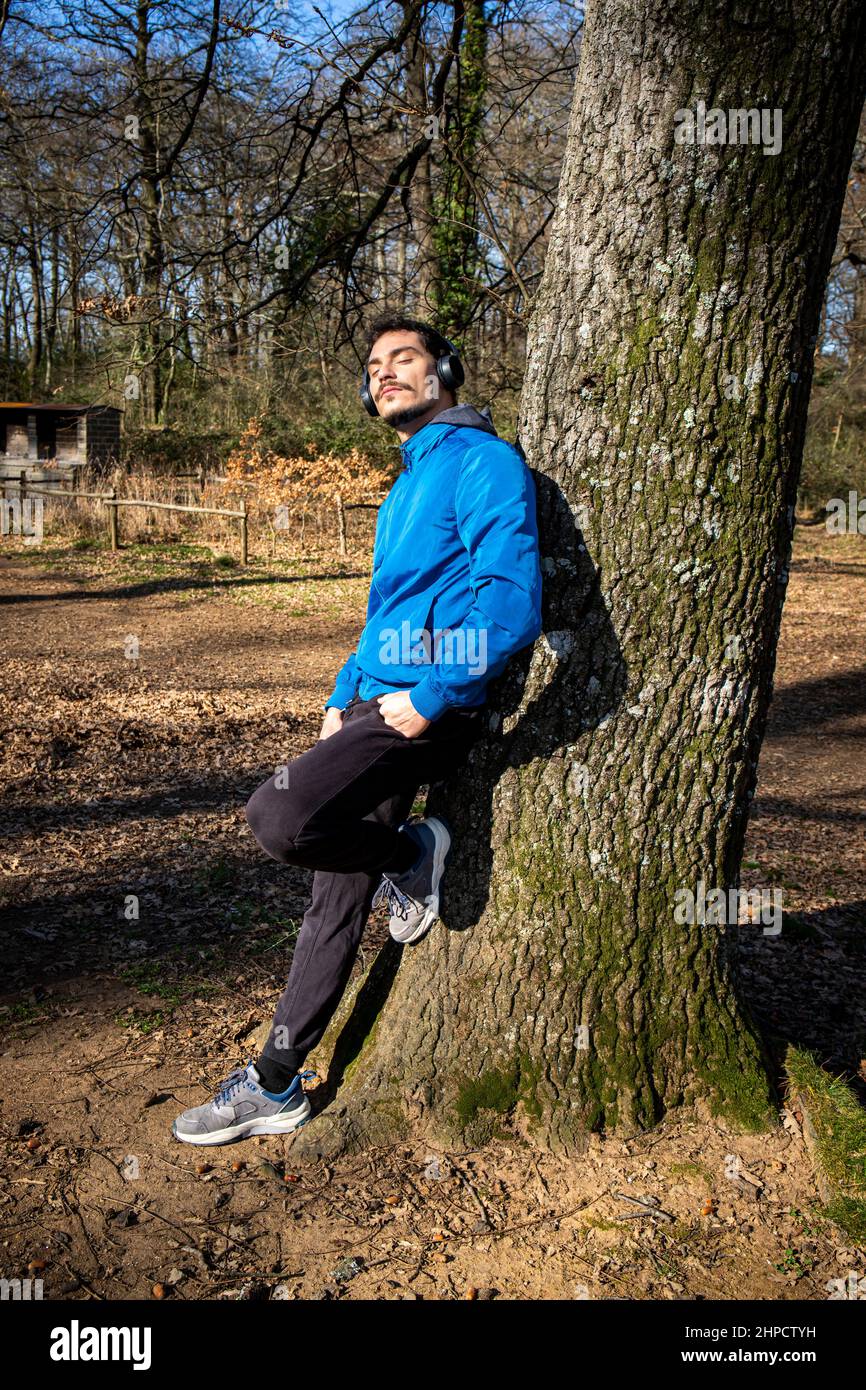 Porträt eines hübschen jungen Mannes mit blauen Augen und einem Schnurrbart, der beim Training Musik hört. Der Mann in der blauen Jacke trainiert in t Stockfoto