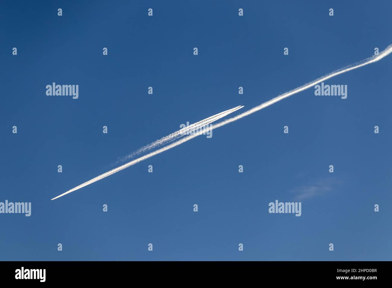 Contrails - zwei Flugzeuge fliegen in entgegengesetzte Richtungen mit weißen Kondensstreifen am blauen Himmel Stockfoto