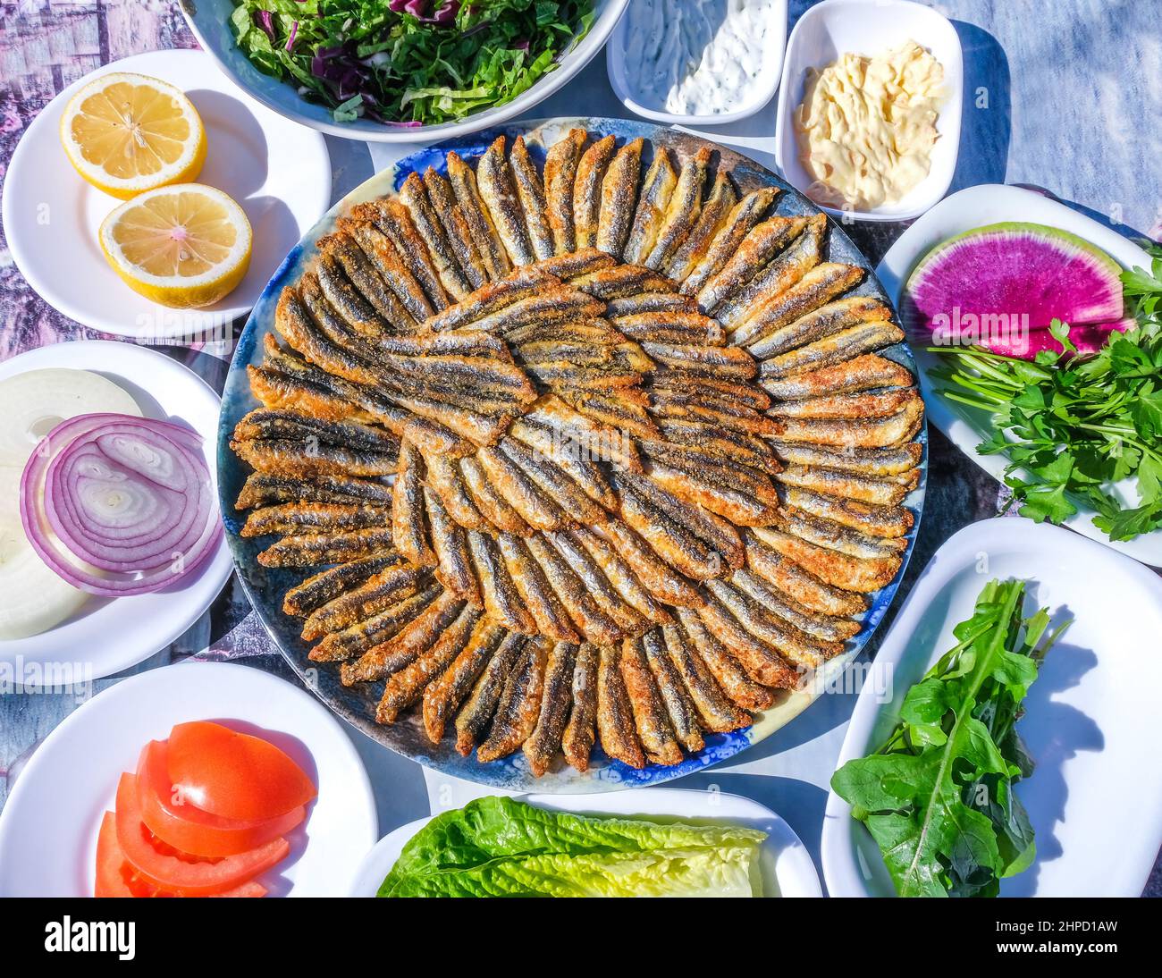 Ein Teller mit frittierten knusprigen Sardellen, türkischer Name Hamsı Tava in Maismehl mit Zitrone, verschiedenen Grüns und Vorspeisen, traditionelle türkische Küche. Stockfoto