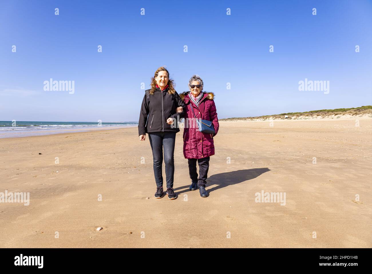 Eine reife Frau, die im Herbst mit ihrer älteren Mutter am Strand spazieren geht Stockfoto