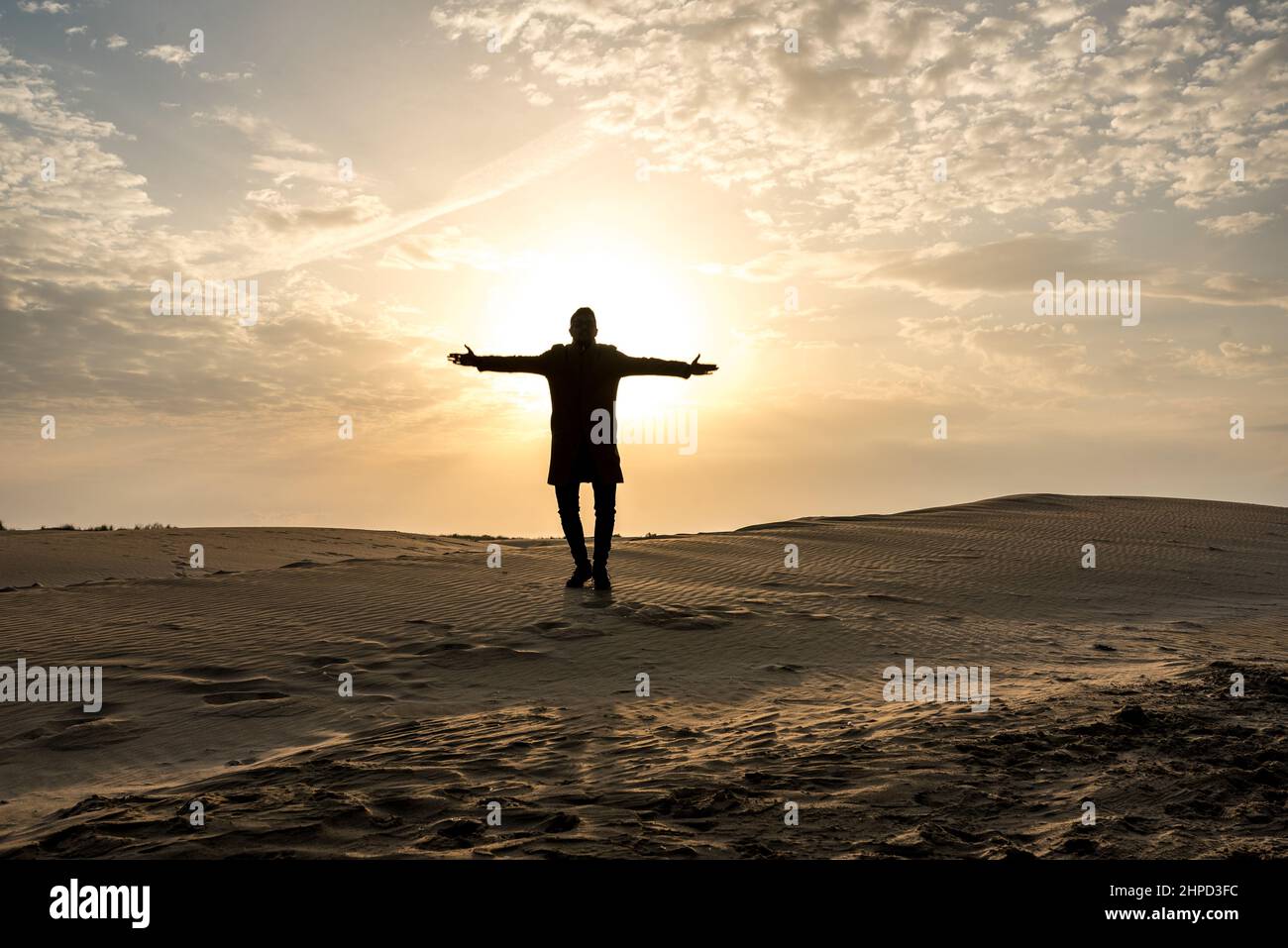 Silhouette eines Mannes mit ausgestreckten Armen auf den Dünen bei Sonnenuntergang. Wüste und Sand. Stockfoto