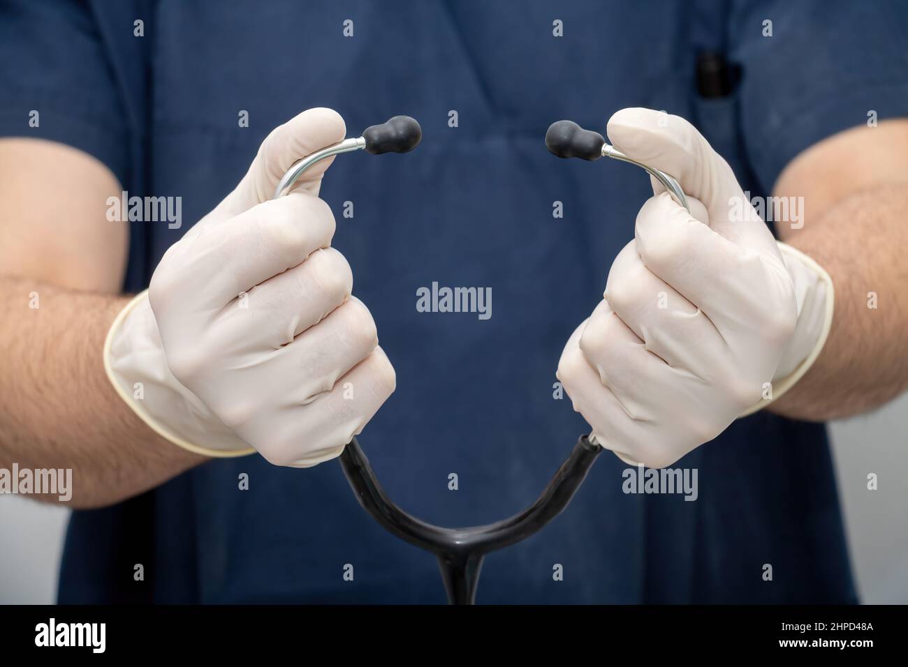 Arzt in medizinischen Uniform hält, in der Hand mit Einweghandschuh, Stethoskop-Schlauch mit Ohrhörer. Gesundheitswesen, Diagnose durch einen Facharzt. Stockfoto