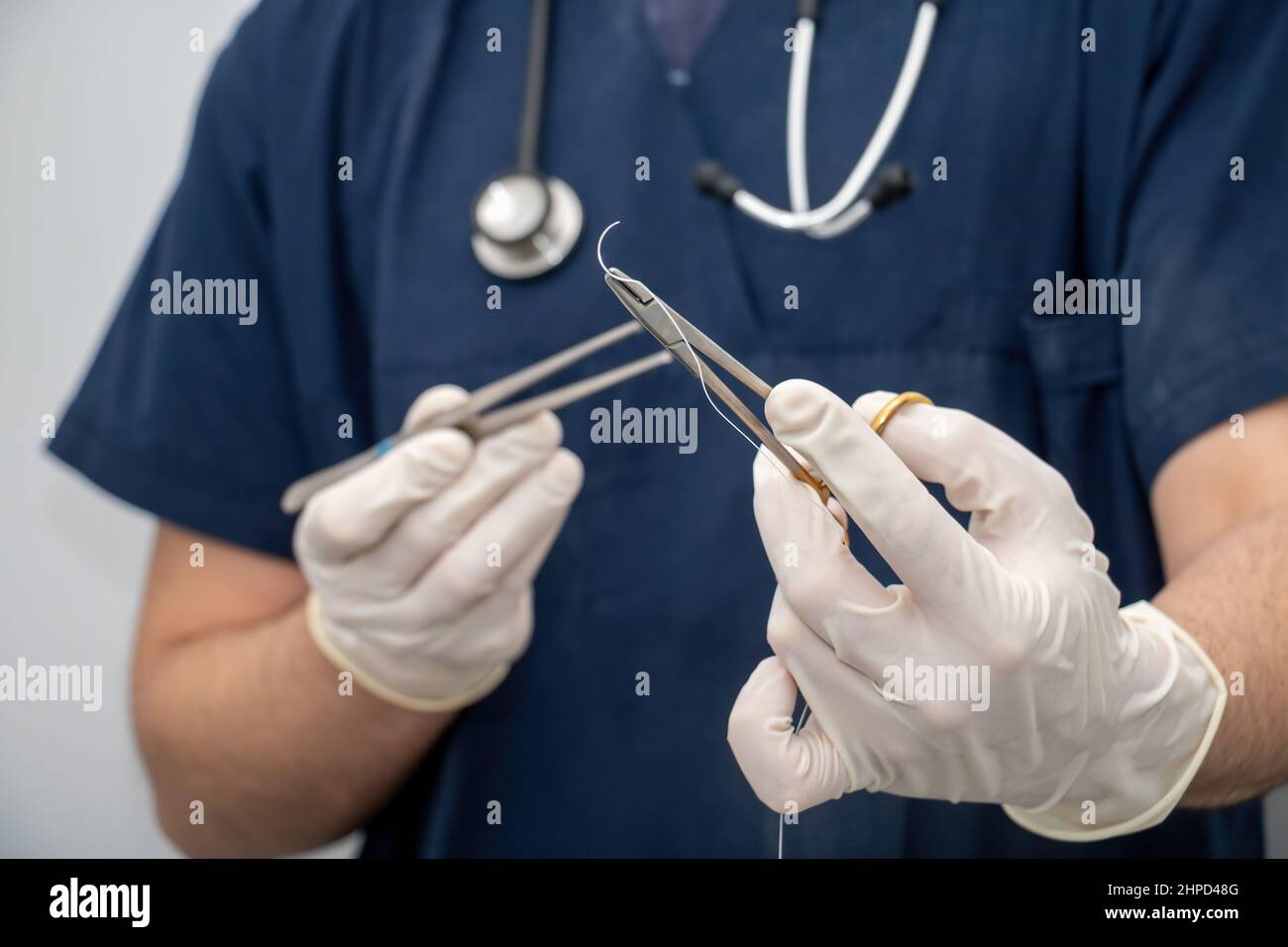 Arzt in medizinischen Uniform hält, in der Hand mit Einweg-Handschuh, chirurgisches Instrument, Nadelhalter und Nahtfaden. Verwischen Sie den Arzt mit der Zeps und Stockfoto