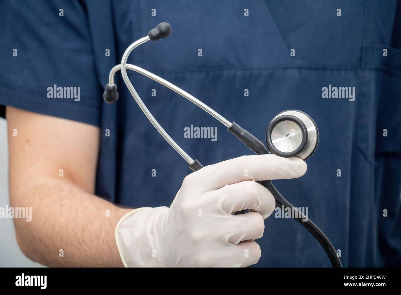 Arzt in medizinischen Uniform hält, in der Hand mit Einweghandschuh, Stethoskop, das aus Disk-förmigen Resonator und Schlauch mit Ohrstück besteht. Gesundheitswesen Stockfoto