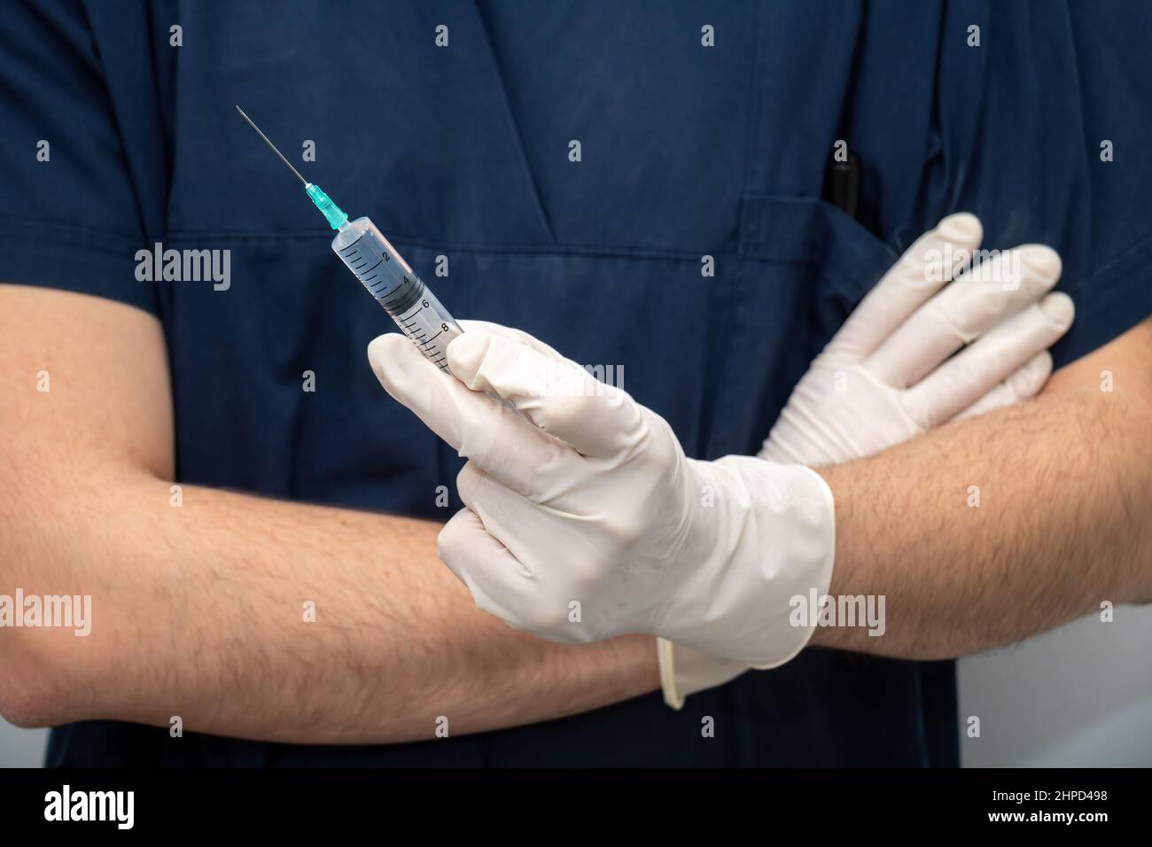 Arzt in medizinischer blauer Uniform mit Einweghandschuh in der Hand, flüssiges Medikament in Spritze mit Nadel. Gesundheitswesen, Behandlung von professionellen phys Stockfoto