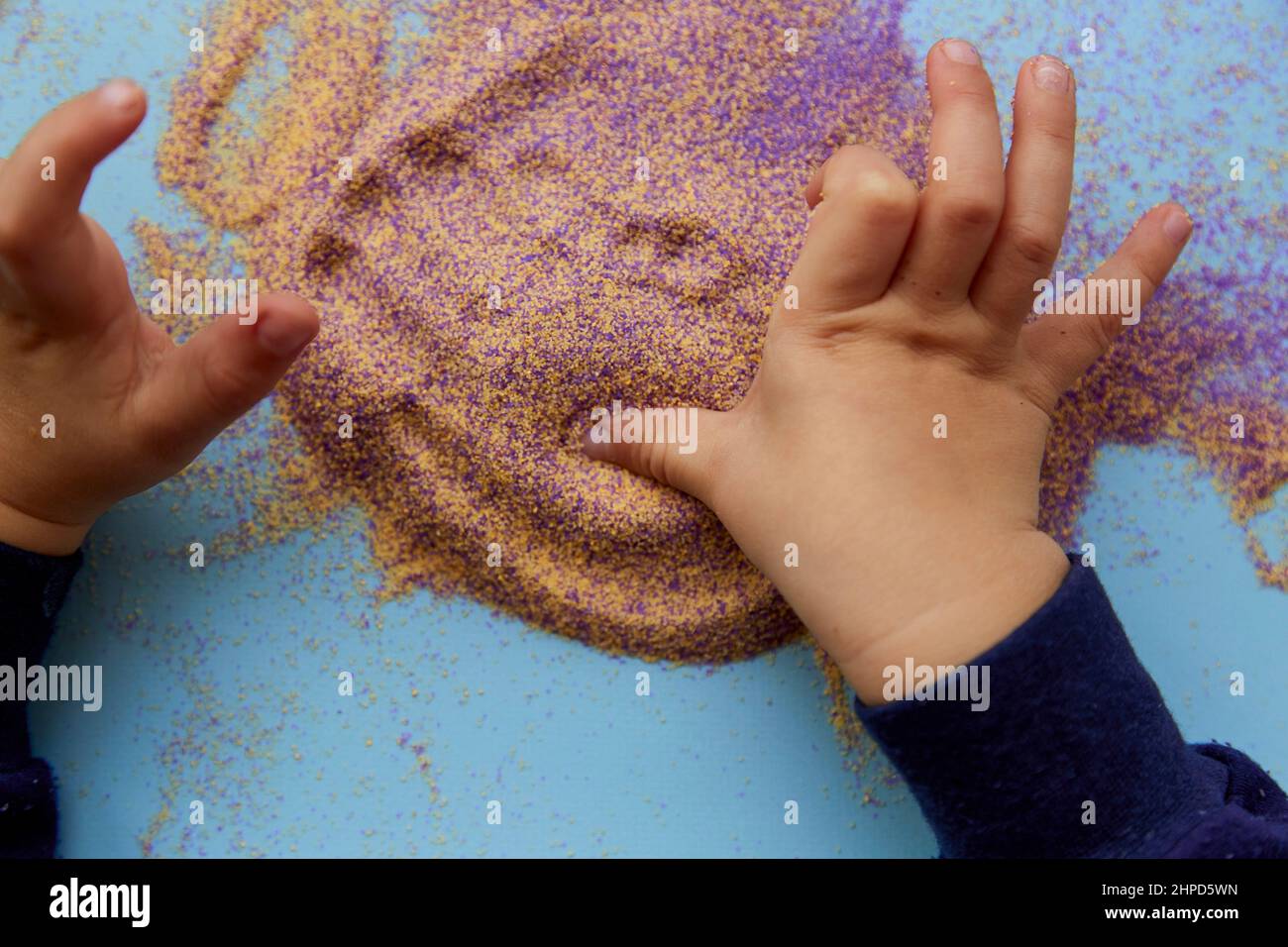 Kinderhände spielen mit buntem Sand. Draufsicht. Entwicklung der Feinmotorik von Kindern. Kreativer Kinderberuf Stockfoto