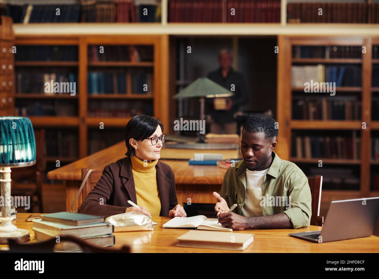 Vorderansicht Porträt von zwei erwachsenen Studenten in der Universitätsbibliothek, die zusammen studieren und einen Laptop benutzen Stockfoto