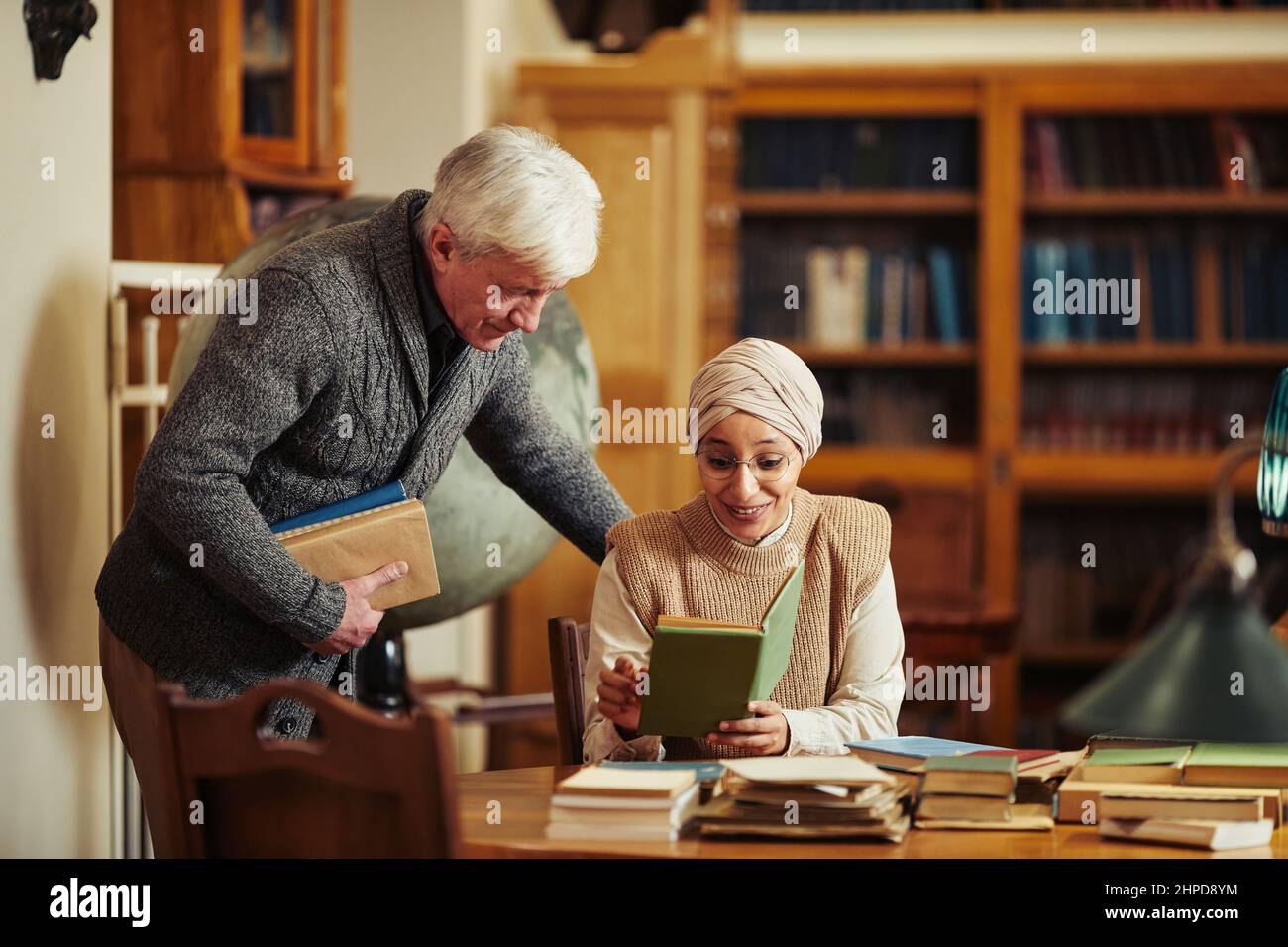 Porträt eines hohen Professors im Gespräch mit einem ethnischen Studenten mit Kopfbedeckung in der klassischen Universitätsbibliothek Stockfoto