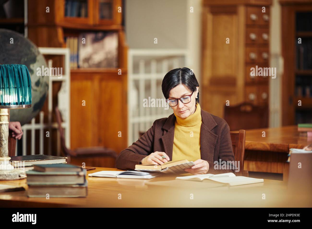 In warmen Farbtönen getragenes Porträt einer eleganten reifen Frau, die in der Bibliothek ein Buch liest, Konzept für Erwachsene Studenten, Kopierraum Stockfoto