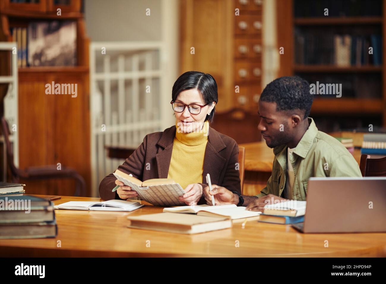 In warmen Farbtönen gehaltene Darstellung einer lächelnden erwachsenen Frau, die in einer College-Bibliothek mit einer afroamerikanischen Freundin studiert Stockfoto