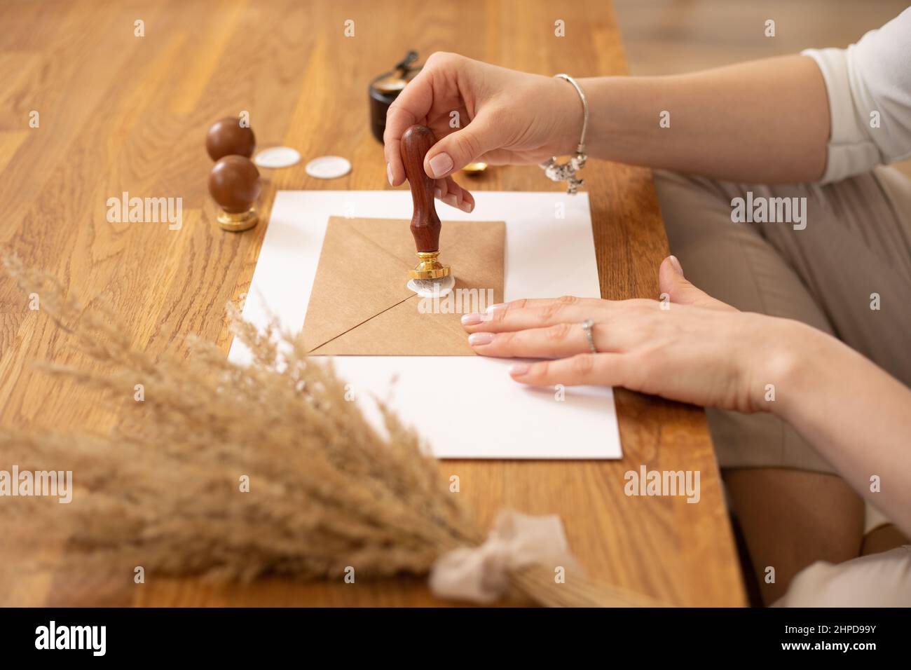 Beschnittenes Foto von Frau Hände, die Zertifikatkarte Briefumschlag Handwerk, sitzen Holzschreibtisch, setzen Siegelwachs drucken Stempel Stockfoto