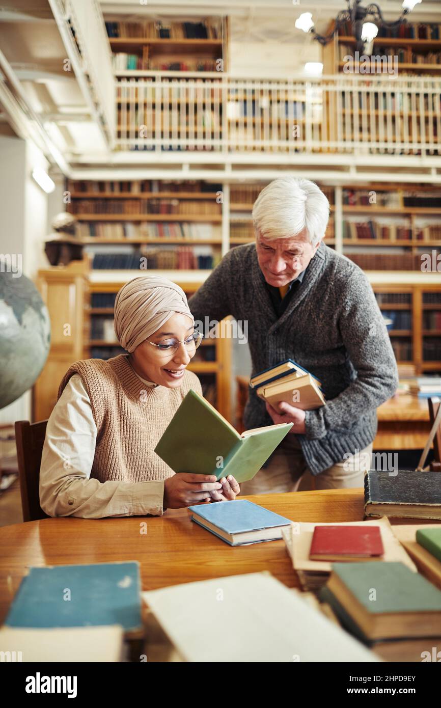 Hochformat Senior Professor im Gespräch mit ethnischen Studenten mit Kopfbedeckung in der College-Bibliothek Stockfoto