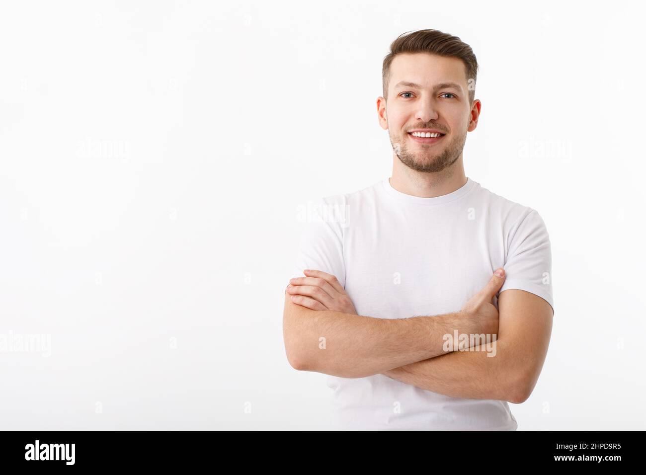 Porträt eines fröhlichen jungen Mannes in einem weißen T-Shirt auf weißem Hintergrund. Der Typ steht und schaut auf die Kamera und lächelt. Stockfoto