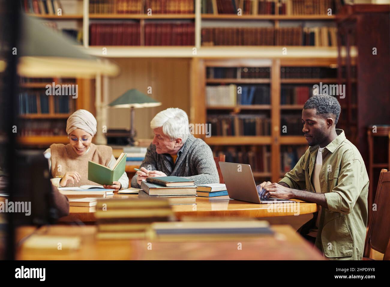 Seitenansicht Porträt eines jungen schwarzen Mannes mit Laptop während des Studiums College-Bibliothek mit Menschen im Hintergrund Stockfoto