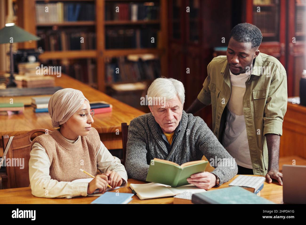Porträt eines weißhaarigen älteren Mannes, der mit zwei jungen Studenten in der Bibliothek studiert Stockfoto