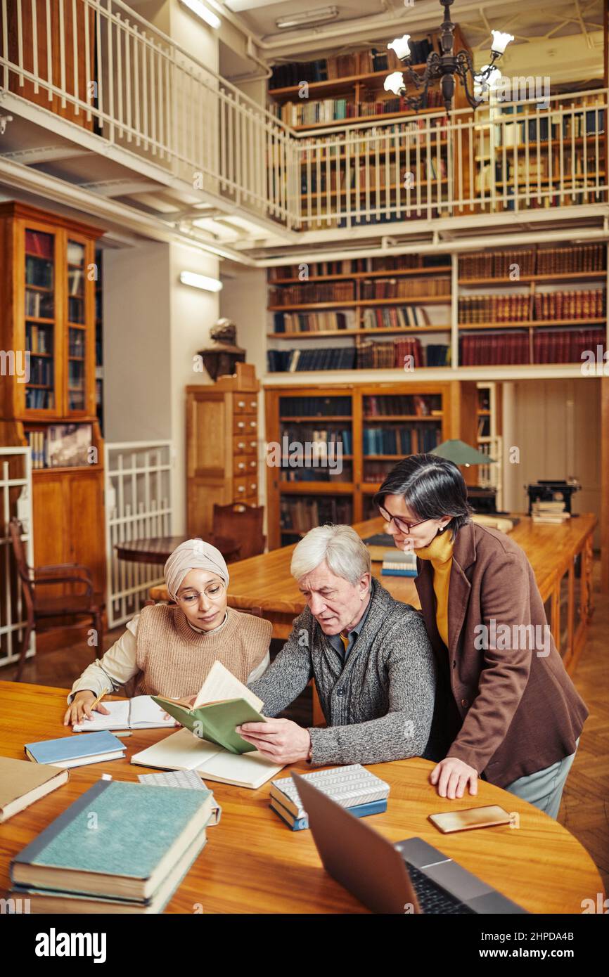 Vertikales Porträt eines weißhaarigen älteren Mannes, der in der Bibliothek mit verschiedenen Studenten studiert, Kopierraum Stockfoto
