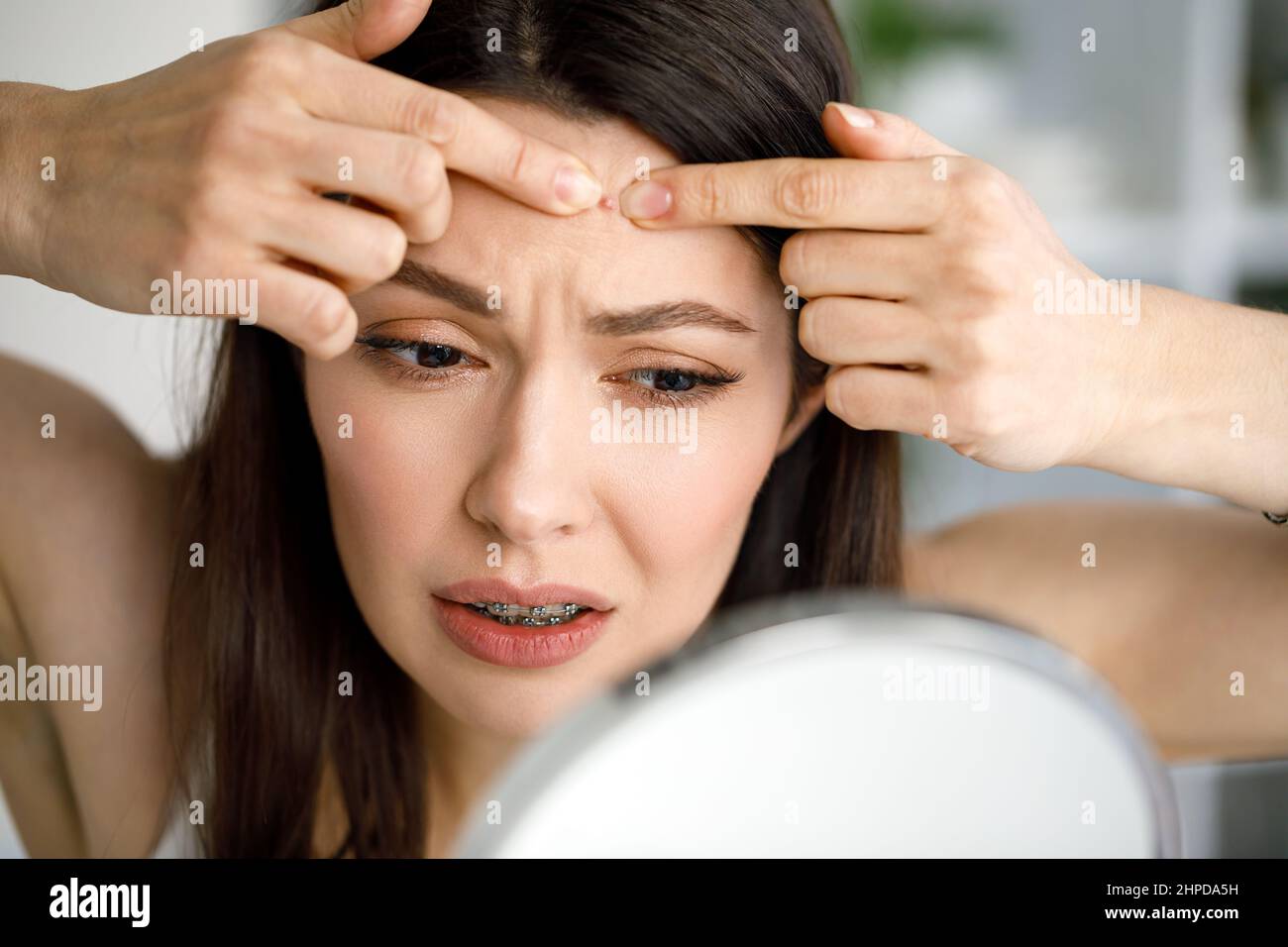 Eine Frau zerquetscht einen Pickel, während sie in den Spiegel schaut. Stockfoto