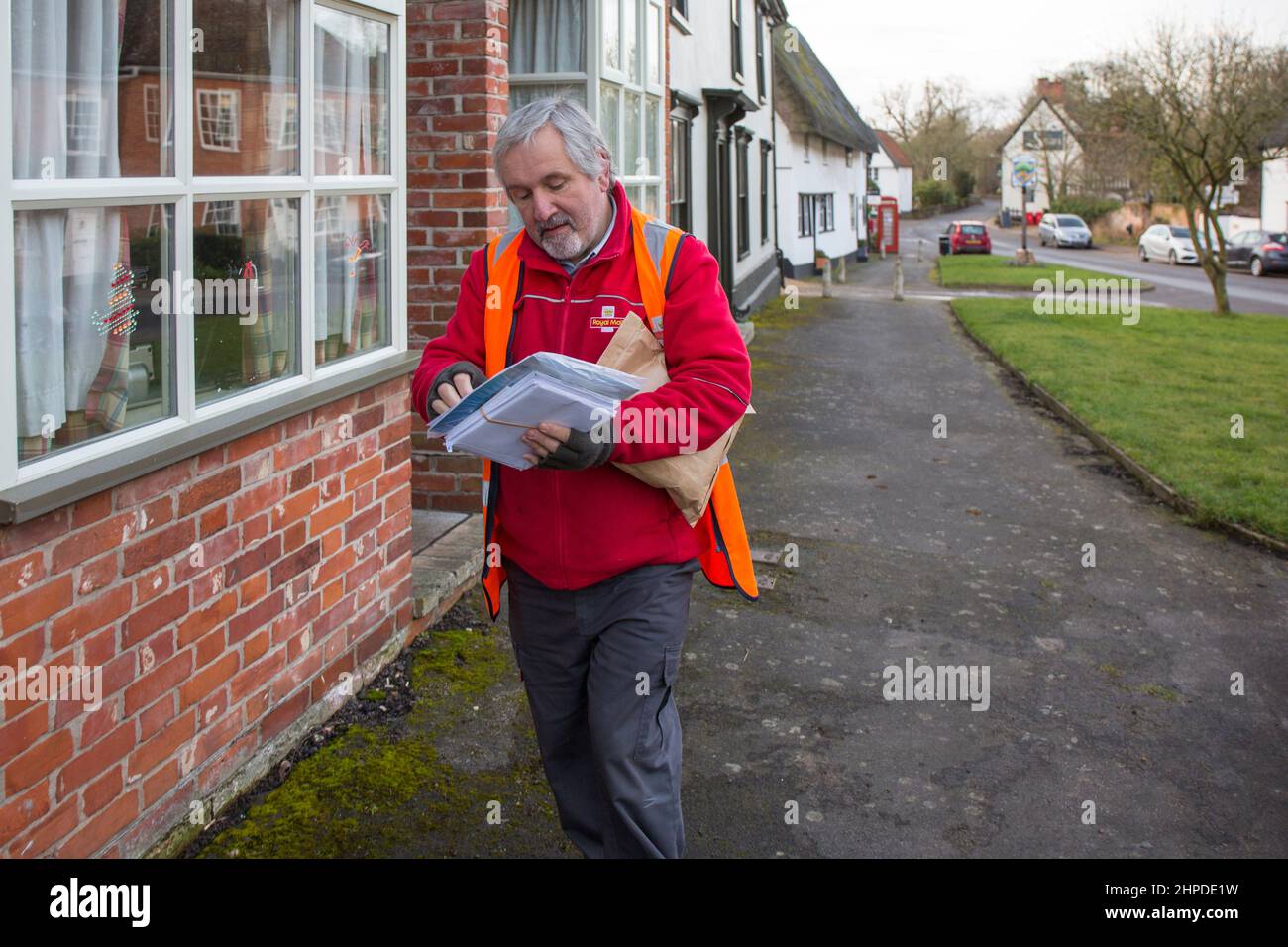 Postbote, der Briefe in einem Suffolk-Dorf, Großbritannien, ausliefert. Stockfoto