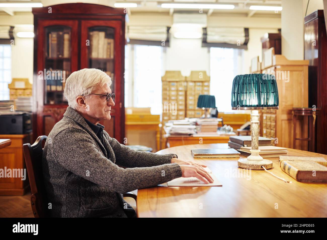 Seitenansicht Porträt eines älteren Mannes mit Sehbehinderung beim Lesen eines Buches in Braille am Tisch in der Bibliothek Stockfoto