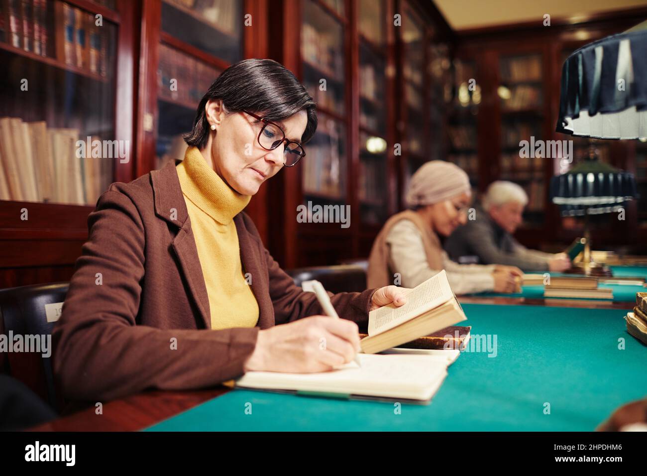 Portrait der erwachsenen Frau, die in der klassischen Bibliothek innen durch Lampe Licht studieren, Raum kopieren Stockfoto