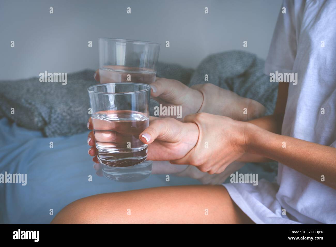 Frau, die ein Glas Wasser in wackeligen Händen hält und an Parkinson-Krankheitssymptomen oder einem wesentlichen Zittern leidet. Stockfoto