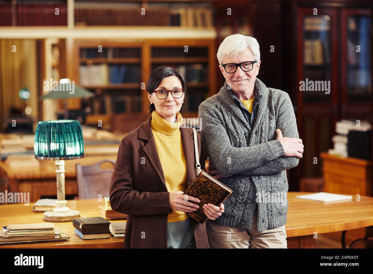 Porträt von zwei Erwachsenen, die Bücher in der klassischen Bibliothek halten und die Kamera betrachten Stockfoto
