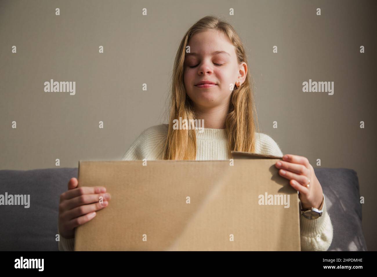 Das Mädchen lächelt und öffnet einen Karton, ein Paket. Stockfoto