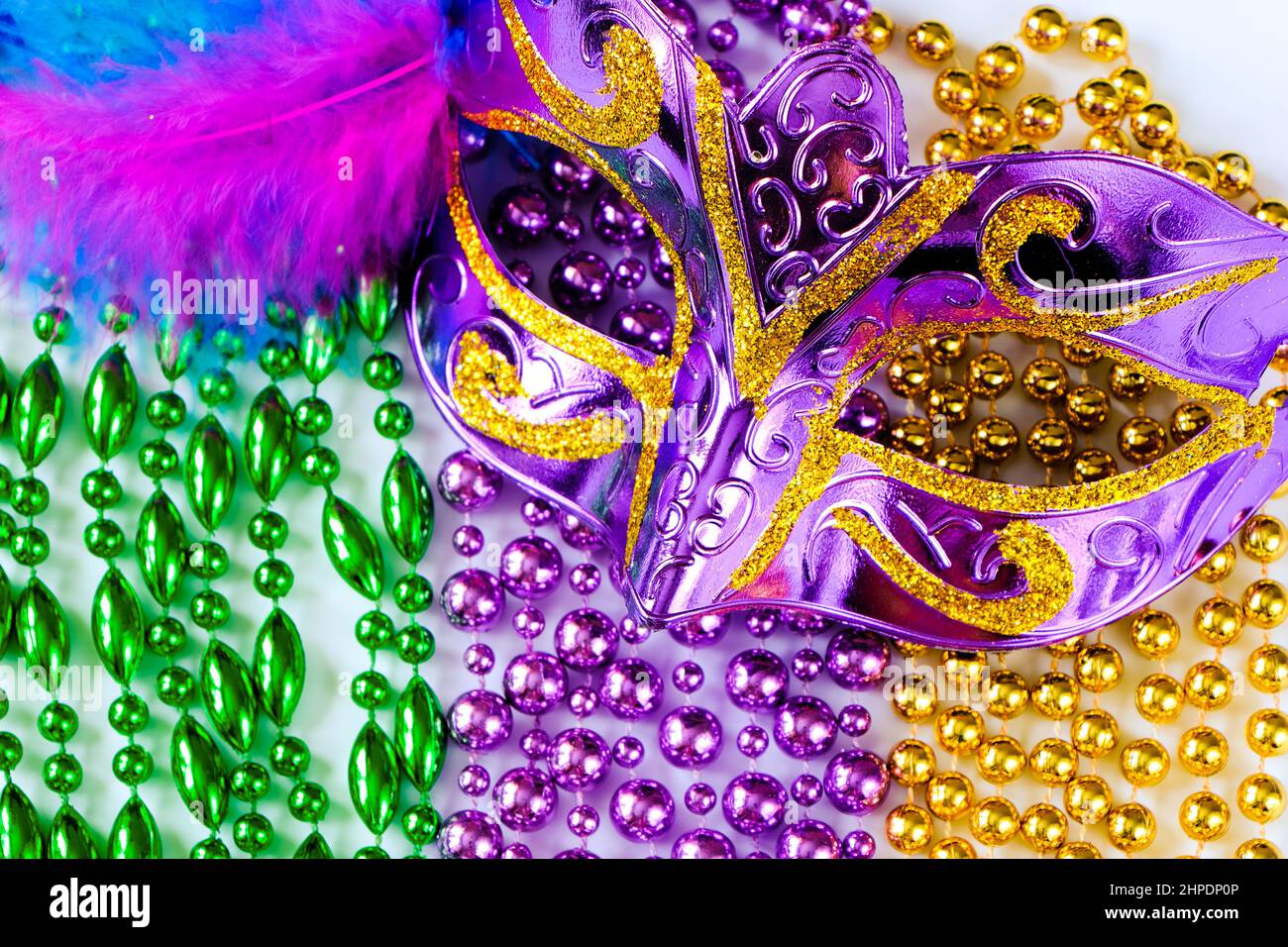 Lila Karnevalsmaske mit Federn und bunten Perlen aus nächster Nähe. Symbol „Mardi Gras“ oder „Fat Tuesday“. Festliche Dekorationen für traditionelle Feiertage. Stockfoto