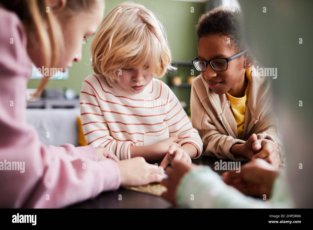 Diverse Gruppe von Kindern spielen mit Puzzle-Spiel drinnen, konzentrieren sich auf blonde kleine Junge, kopieren Raum Stockfoto