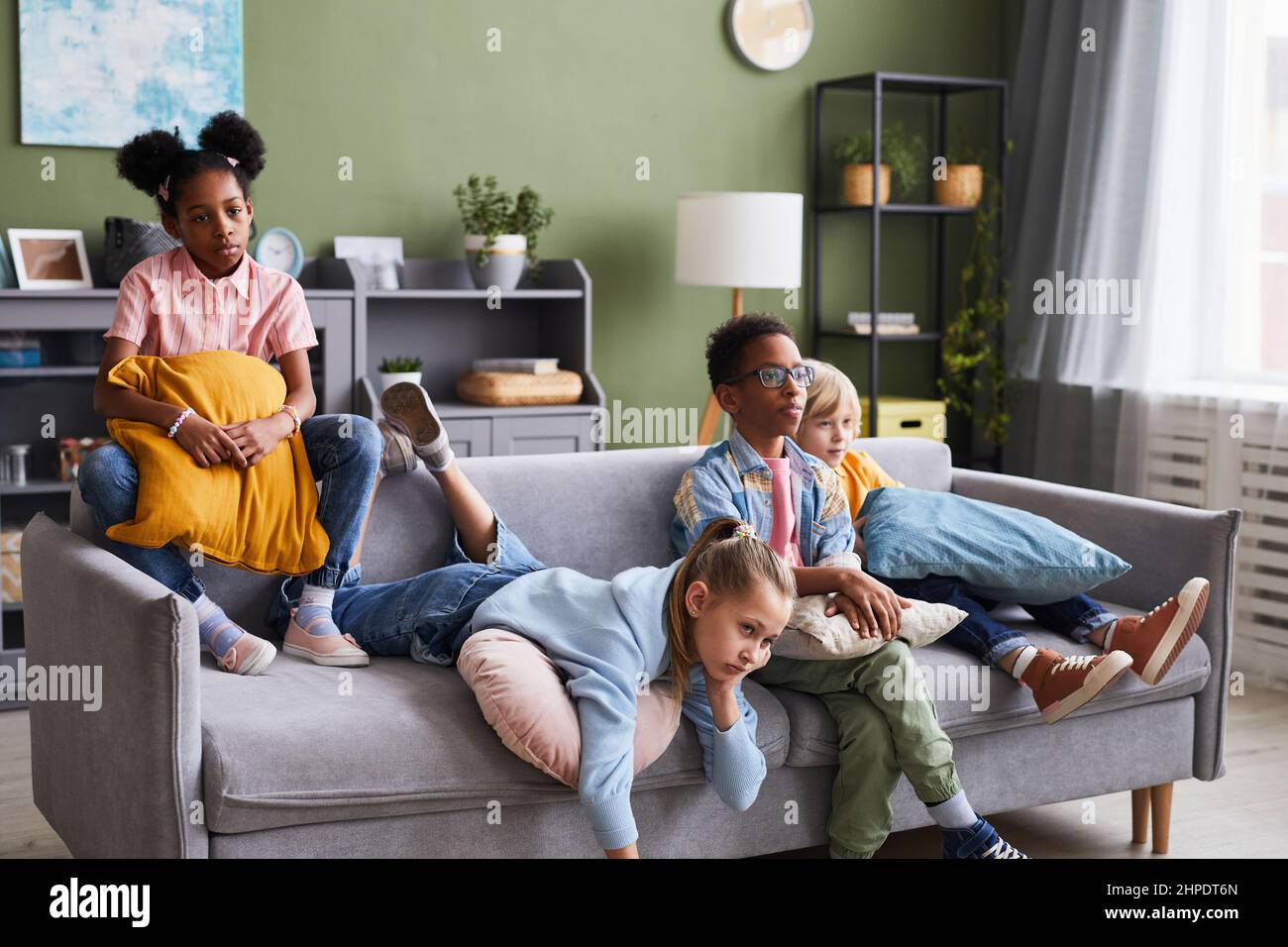 Eine vielfältige Gruppe von Kindern, die zu Hause Fernsehen, während sie sich auf dem Sofa entspannen und langweilig aussehen Stockfoto