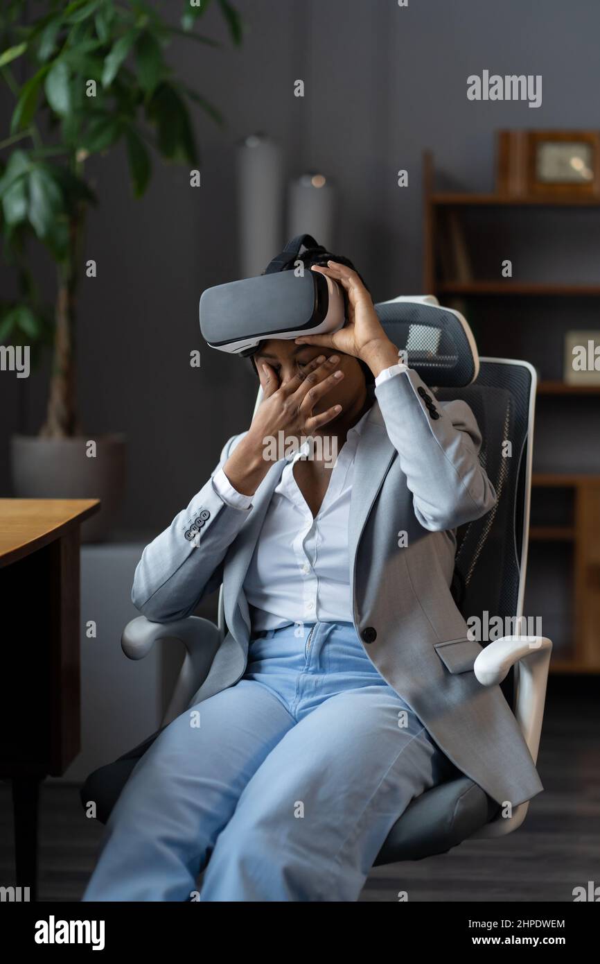 Frustrierte afrikanische Geschäftsfrau reibt müde Augen, weil sie im Büro für die Arbeit eine VR-Brille trägt Stockfoto