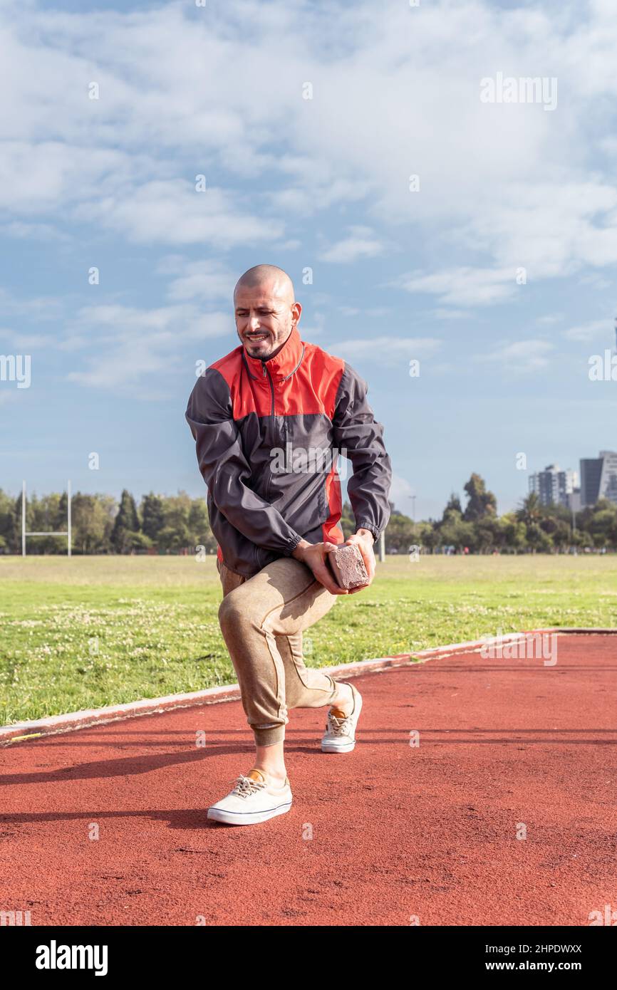 Junger kahlköpfiger Sportler, der mit einem Backstein im Freien in einem Park funktionelle Übungen macht Stockfoto