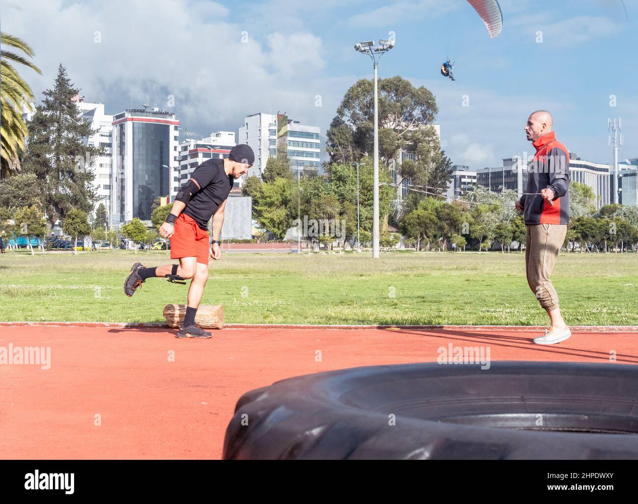 Zwei junge Athleten machen funktionelle Übungen, springen Seil und laufen in einem Park mit einem Gleitschirm, der am Himmel fliegt Stockfoto