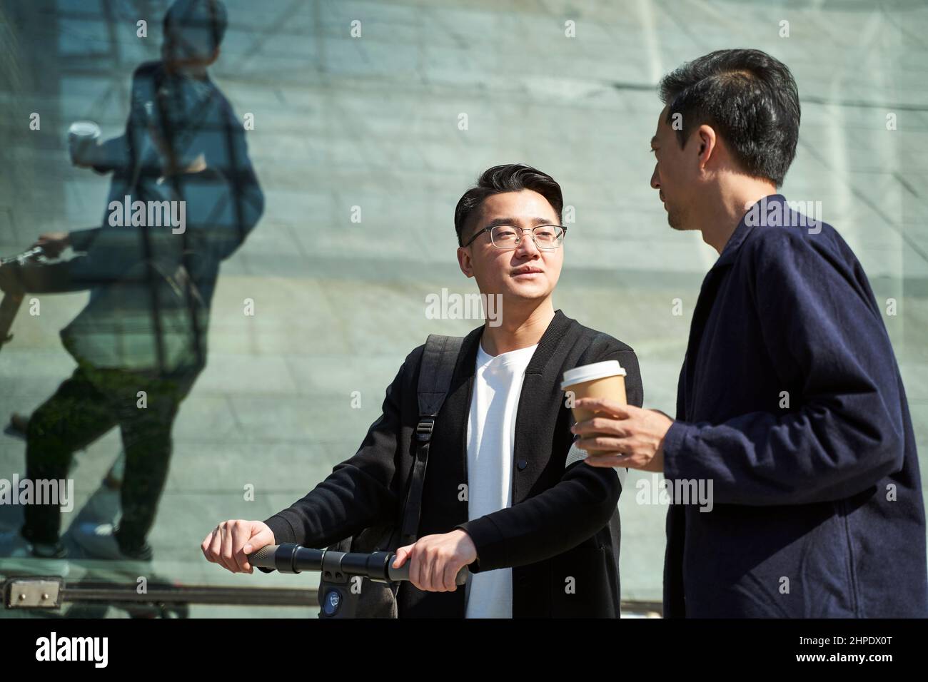 Zwei junge asiatische Freunde, Kollegen, unterhalten sich beim Gehen auf der Straße Stockfoto