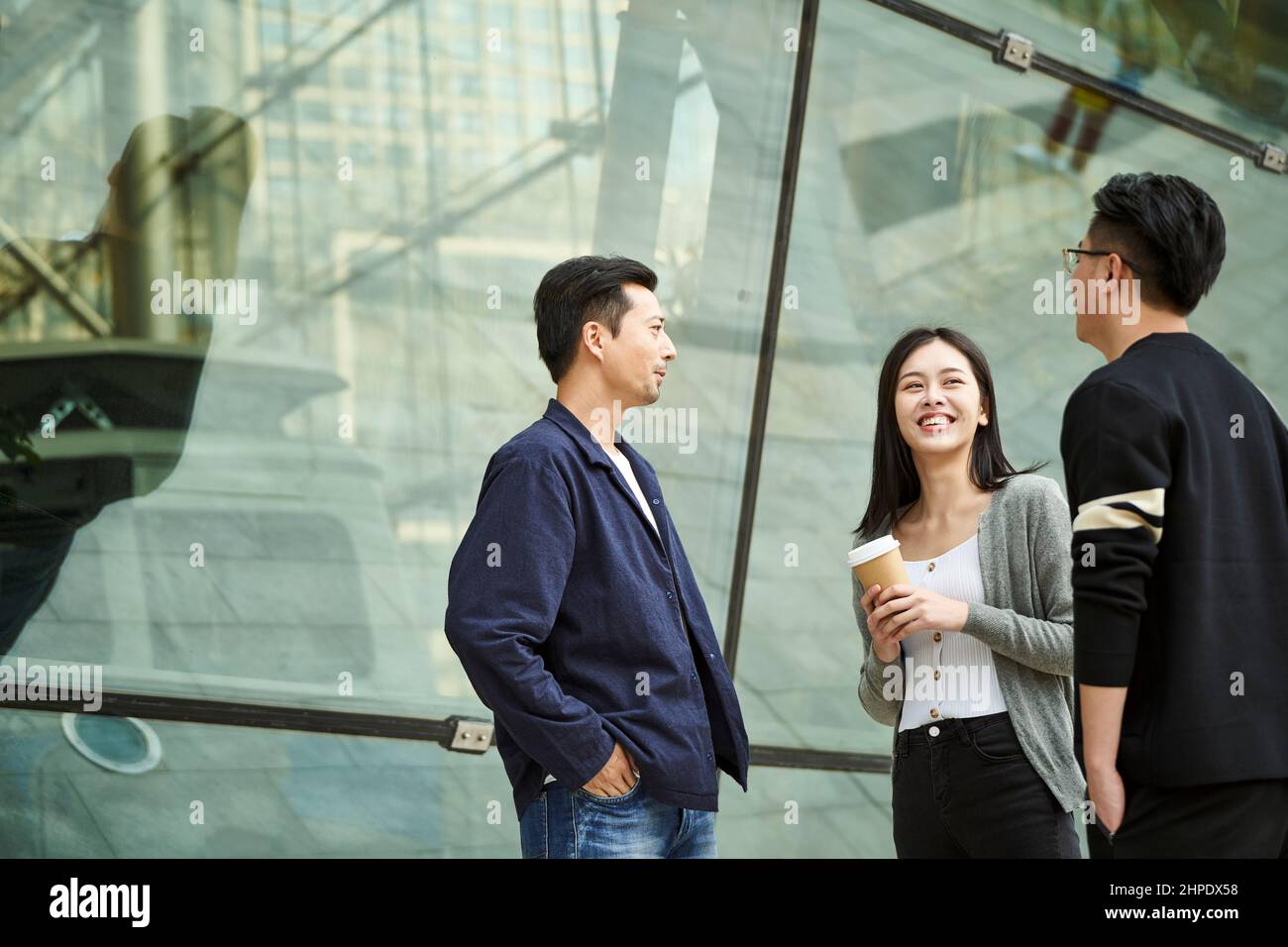Drei junge asiatische Menschen stehen und unterhalten sich glücklich und lächelnd auf der Straße Stockfoto