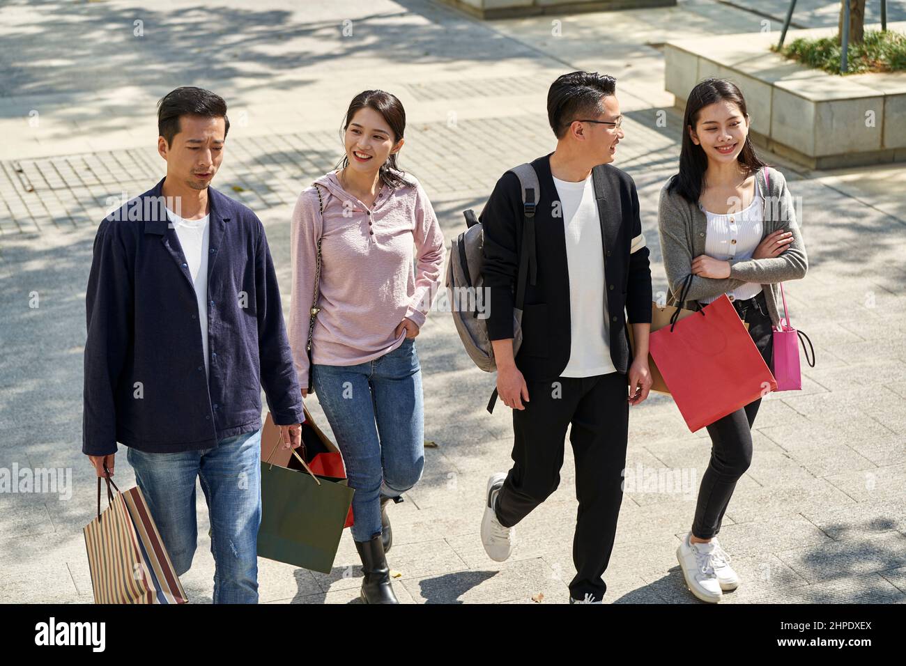 Aus der Perspektive einer Gruppe von vier jungen asiatischen Menschen, die sich unterhalten und sich unterhalten, während sie mit Einkaufstaschen in den Händen auf der Straße spazieren Stockfoto